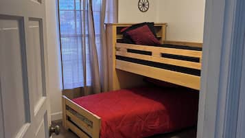 Una habitación con literas, ventilador de techo, alfombra de cuero y una ventana con cortinas.