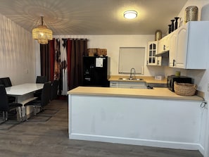 A compact kitchen with a dining area, featuring a refrigerator, microwave, sink, and a chandelier. - Rudolph’s Rustic Charming 3-bedroom Western Oasis in beautiful Pahokee (Pahokee)