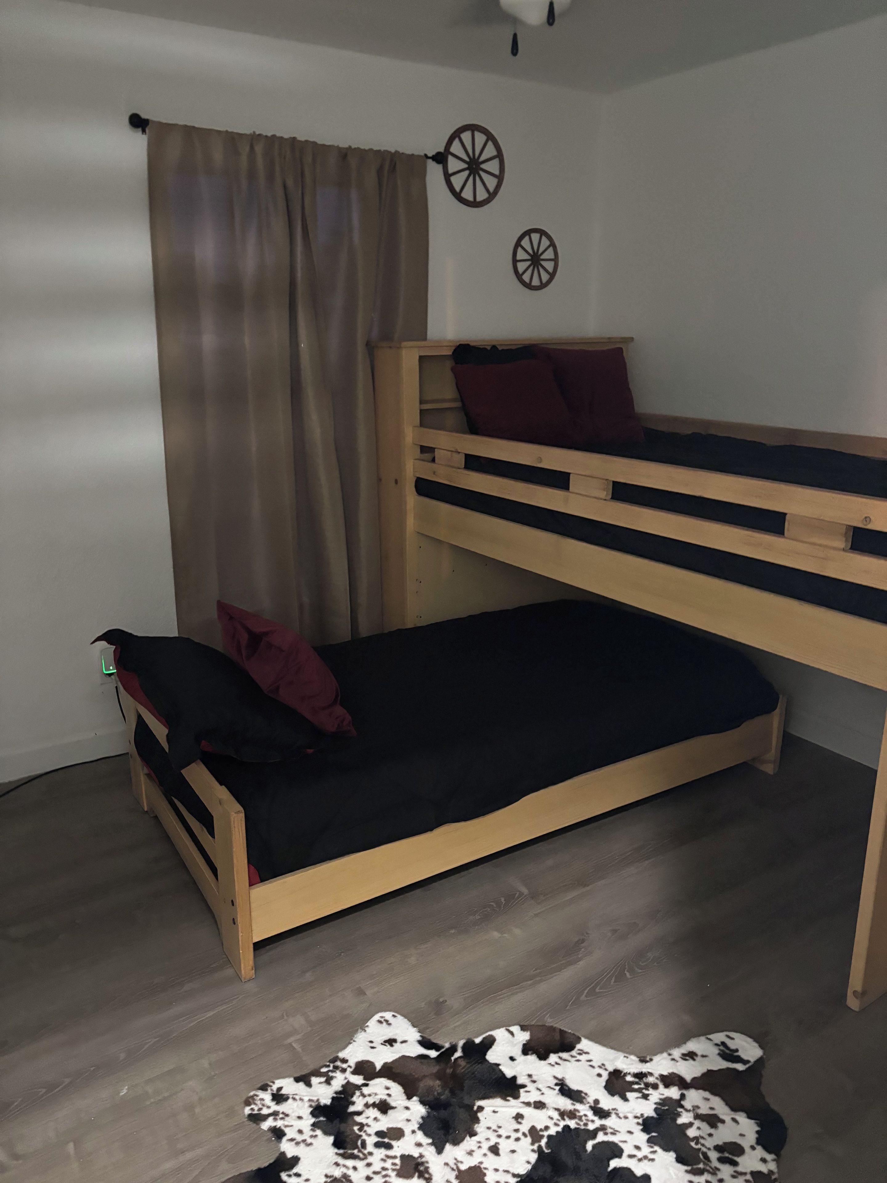 Ein Etagenbett mit dunkler Matratze und rotem Kopfkissen, Holzboden und ein Kuhfellteppich.