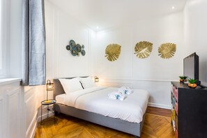 A modern bedroom with a grey bed, white bedding, decorative wall art, a bedside lamp, and a wooden floor. - Welcoming Apartment -1br/6p - Auteuil / Passy (Paris)