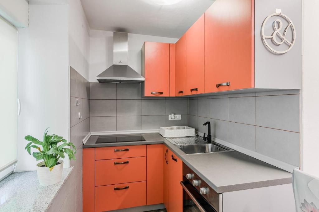Una cocina compacta con armarios naranjas, un lavamanos de acero inoxidable y una estufa moderna.