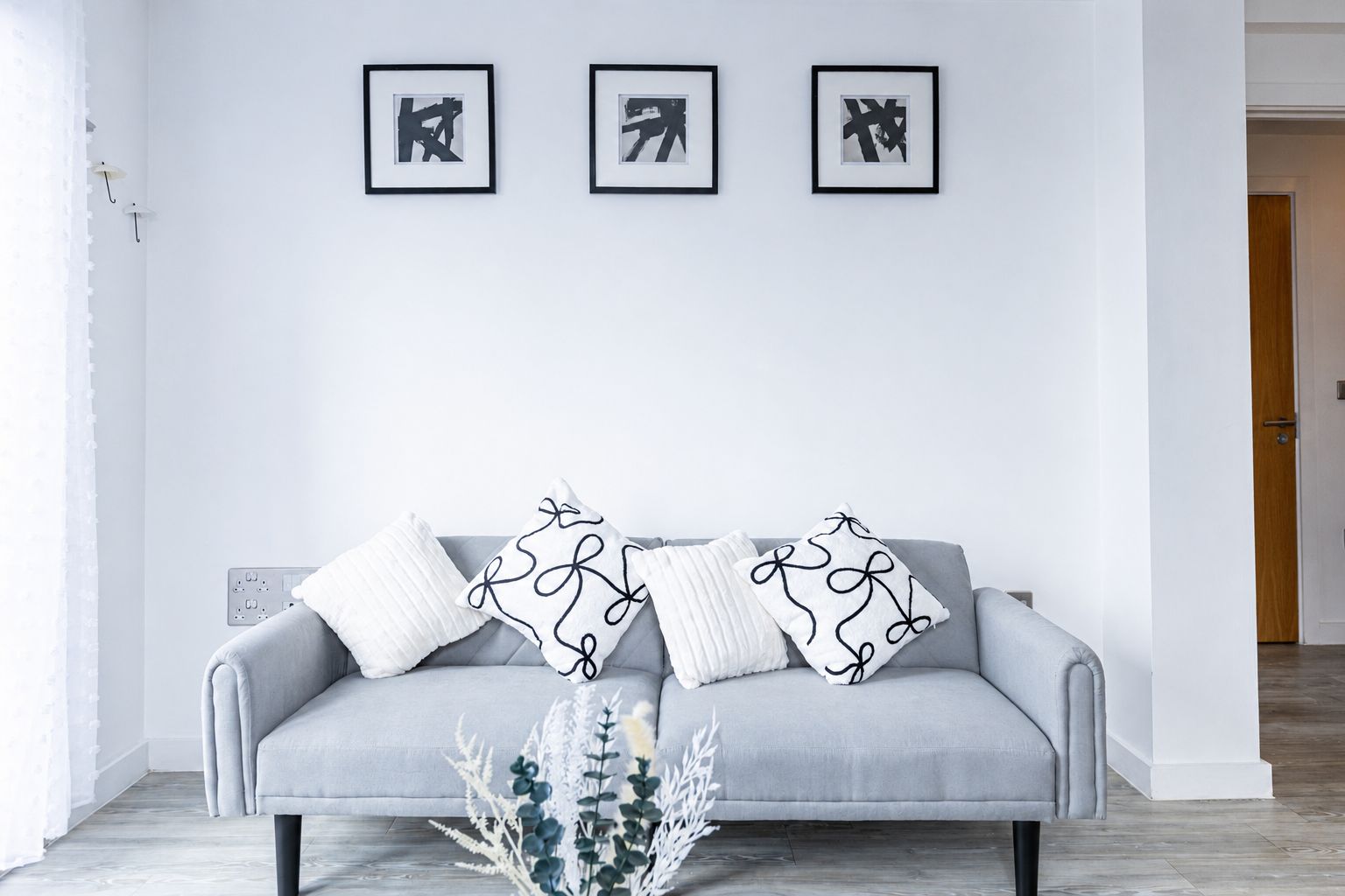 A grey sofa with patterned pillows, a white wall, and three framed abstract artworks.