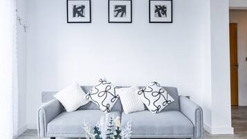 A grey sofa with patterned pillows, a white wall, and three framed abstract artworks.
