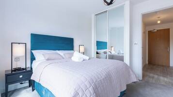 A hotel room with a large bed, bedside tables, a mirror, and a door leading to another room.