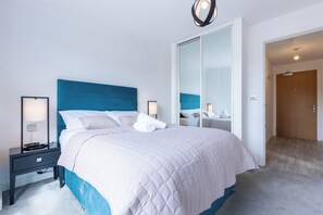 Ein Hotelzimmer mit einem großen Bett, Nachttischen, einem Spiegel und einer Tür zu einem weiteren Raum.