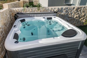 A hot tub with multiple jets, set against a stone wall and a grassy area. - Apartment Break with Private jacuzzi (Novalja)