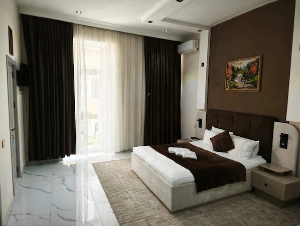 Una habitación de hotel moderna con una cama grande, una mesita de noche, un cuadro en la pared y vistas al exterior por la ventana.