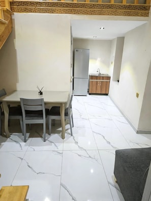Una cocina compacta con refrigerador, gabinetes de madera y piso de mármol.