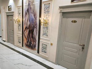Un pasillo con suelo de mármol, un cuadro grande en la pared y dos puertas con placas de número.