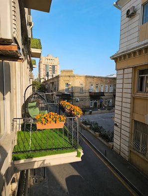 Un balcón con una silla metálica, una maceta con flores y vista a una calle de la ciudad.