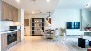 A modern kitchen with built-in appliances, a dining area with a round table and chairs, and a living room with a flat-screen TV. - Luxurious 1BR apartment in Beach Vista, beach access, EMAAR Beachfront Harbour (Dubai)