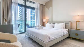Een hotelkamer met een groot bed, twee nachtkastjes, een stoel en uitzicht op de stad door middel van kamerhoge ramen.