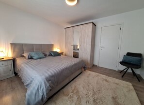 Un dormitorio con cama, lámparas de noche, un armario, una silla y una puerta.