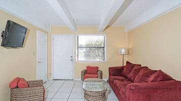 A living room with a television, a sofa, a chair, a small table, and a window with blinds.