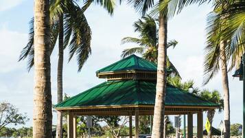 A gazebo with a green roof, surrounded by palm trees and a gravel path.
