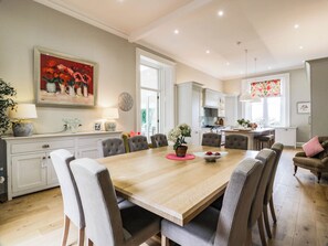 A dining area with a wooden table, six upholstered chairs, a vase with flowers, and a clock on the wall. - Eagle Glen Manor House (Blairgowrie)