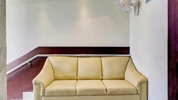 A beige sofa in a lobby area with a staircase in the background.