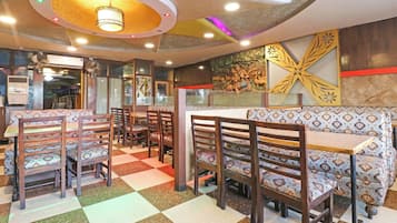 Interior de restaurante con cabinas, sillas de madera, cojines estampados, piso a cuadros y techo decorativo.