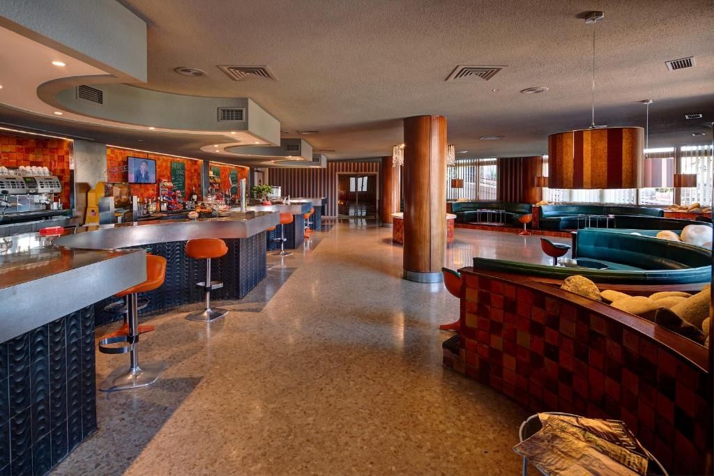 A modern bar area with a counter, stools, and a seating area with sofas and a large pillar.