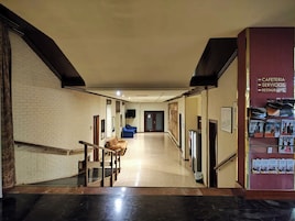 Vestíbulo de hotel con una escalera, un mostrador de recepción y una pared con indicaciones.