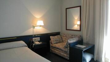 A hotel room with a bed, a chair, a desk, a telephone, and a mirror.