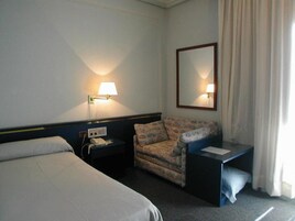 Una habitación de hotel con una cama, una silla, un escritorio, un teléfono y un espejo.