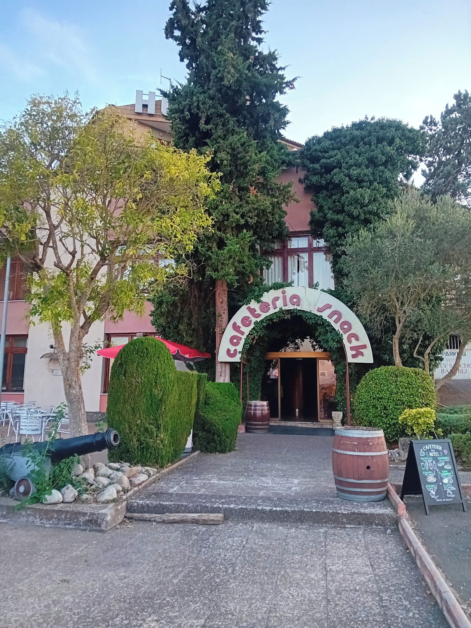 Entrada de un edificio con un cartel que dice 'Cafetería snack' y un gran arco.