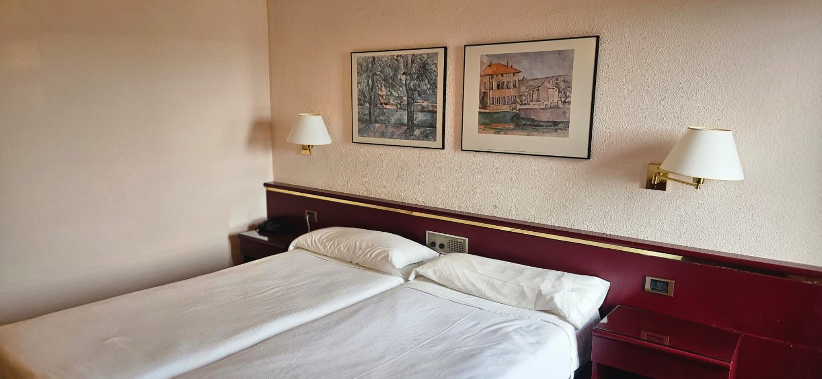 A hotel room with a bed, two wall-mounted lamps, and two framed pictures.