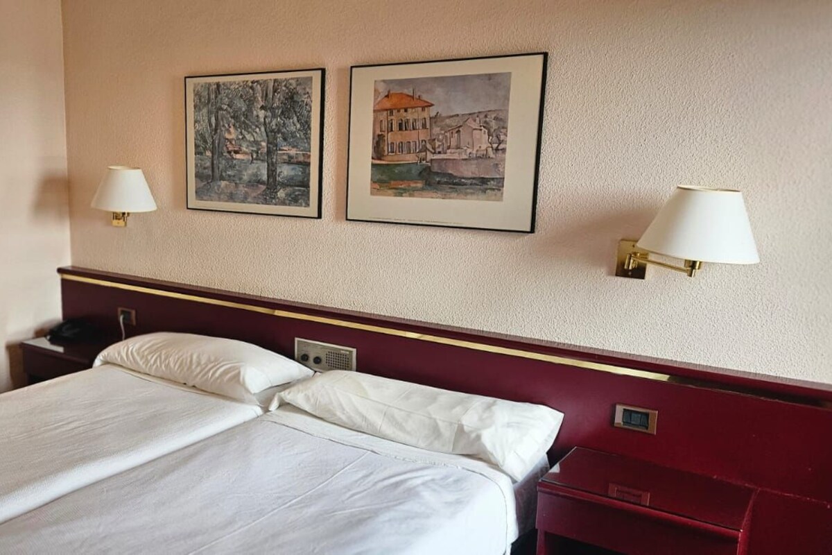 Quarto de hotel com uma cama, duas luminárias fixadas na parede e duas quadros emoldurados.