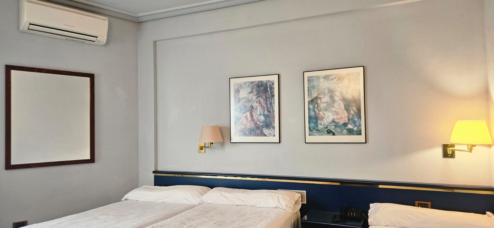 A hotel room with a bed, two wall-mounted lamps, and two framed artworks.