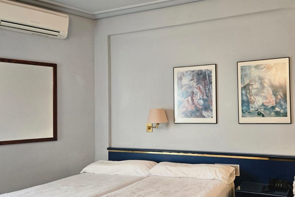Quarto de hotel com uma cama, duas luminárias fixadas na parede e duas obras de arte emolduradas.