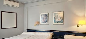 Una habitación de hotel con una cama, dos lámparas fijadas a la pared y dos obras de arte enmarcadas.