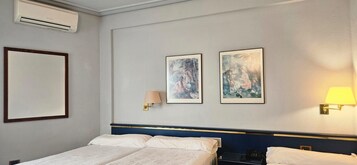 Una habitación de hotel con una cama, dos lámparas fijadas a la pared y dos obras de arte enmarcadas.