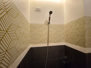 A corner bathroom with a shower, dark tiles, and a geometric patterned wall. - Liz's Urban Deca Cubao Studio Unit (Quezon City)