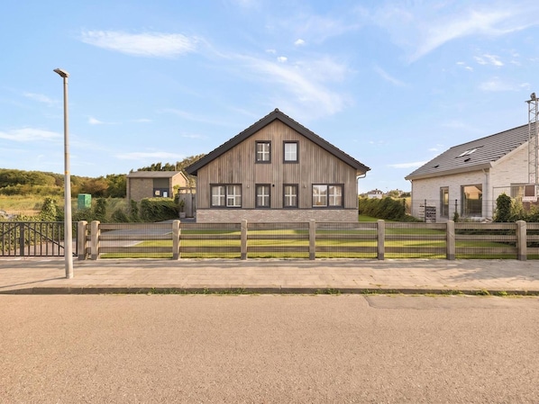 En moderne boligbygning i to etager med skråtag, en indhegnet forhave og en gadelampe.