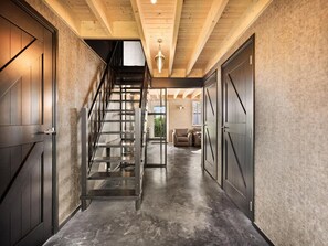 A modern interior with a staircase leading to a loft area, a seating area with a sofa and chairs, and a large door on the right. - Luxurious Home Behind the Dunes of Julianadorp (Julianadorp)
