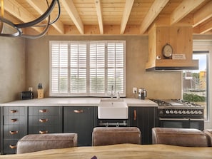 A kitchen with a central island, wooden cabinets, a stove, and a window with blinds. - Luxurious Home Behind the Dunes of Julianadorp (Julianadorp)