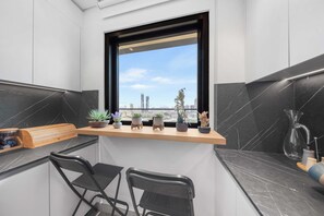 A modern kitchen with a black and white color scheme, a window with a city view, and a bar area with chairs. - Designer 1BR, Pool View, Finest Renovation JVC (Dubai)