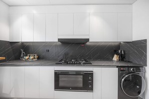 A compact kitchen with a gas stove, oven, and built-in washing machine. - Designer 1BR, Pool View, Finest Renovation JVC (Dubai)