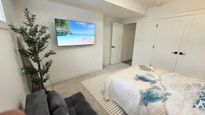 Un dormitorio con una cama, un televisor en la pared, una planta y una puerta.