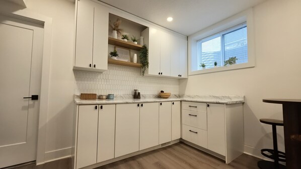 Una cocina con armarios blancos, encimera de madera y ventana con persianas.