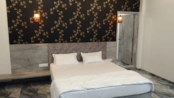 Un dormitorio con una cama, dos almohadas, suelo de mármol, pared de un diseño oscuro y dos luces fijadas a la pared.