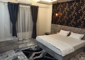 A hotel room with a bed, curtains, a patterned wall, and a nightstand.