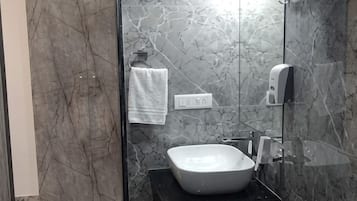 Un baño moderno con pared de mármol, un lavamanos blanco, un perchero y un cabezal de ducha de mano.