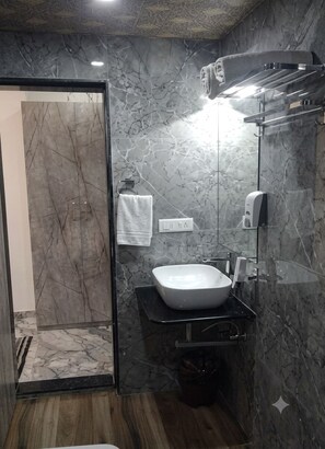 Een moderne badkamer met een marmeren wand, een witte wastafel, een handdoekhouder en een handdouche.
