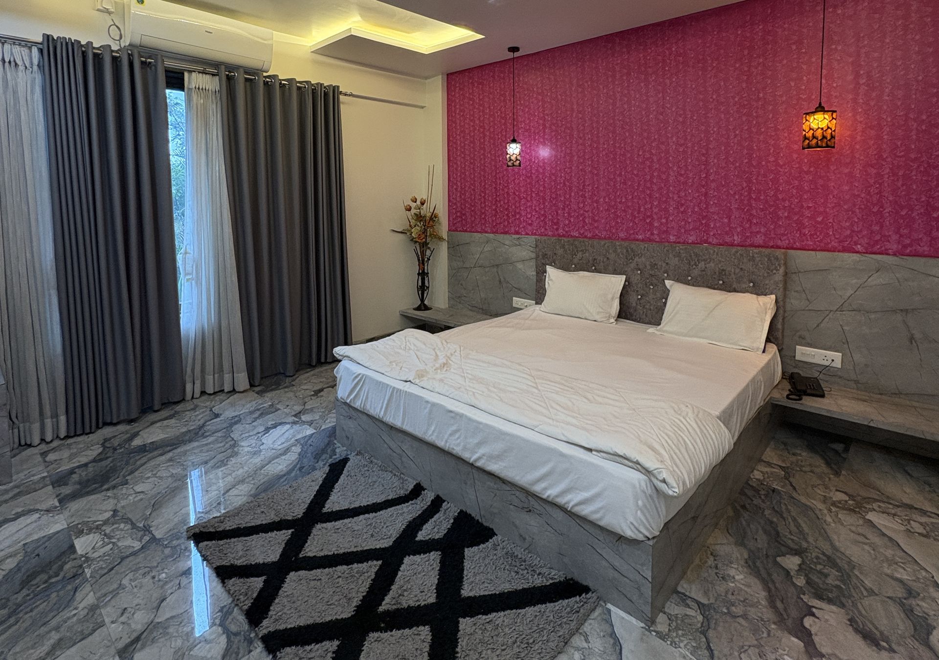 A modern bedroom with a marble floor, a large bed, a nightstand, a vase with flowers, and a pink textured wall.
