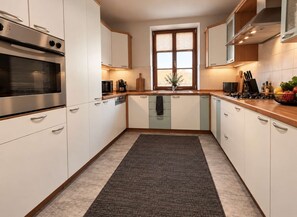 Eine moderne Küche mit weißen Schränken, einer zentralen Kochinsel, einem eingebauten Backofen und einem Fenster, das für natürliches Licht sorgt.