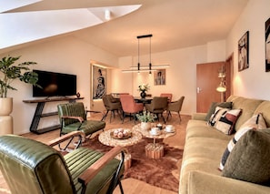 Ein modernes Wohnzimmer mit einem Flachbildfernseher, Ledersesseln, einem Couchtisch mit Dekoration und einer Couch mit Kissen.