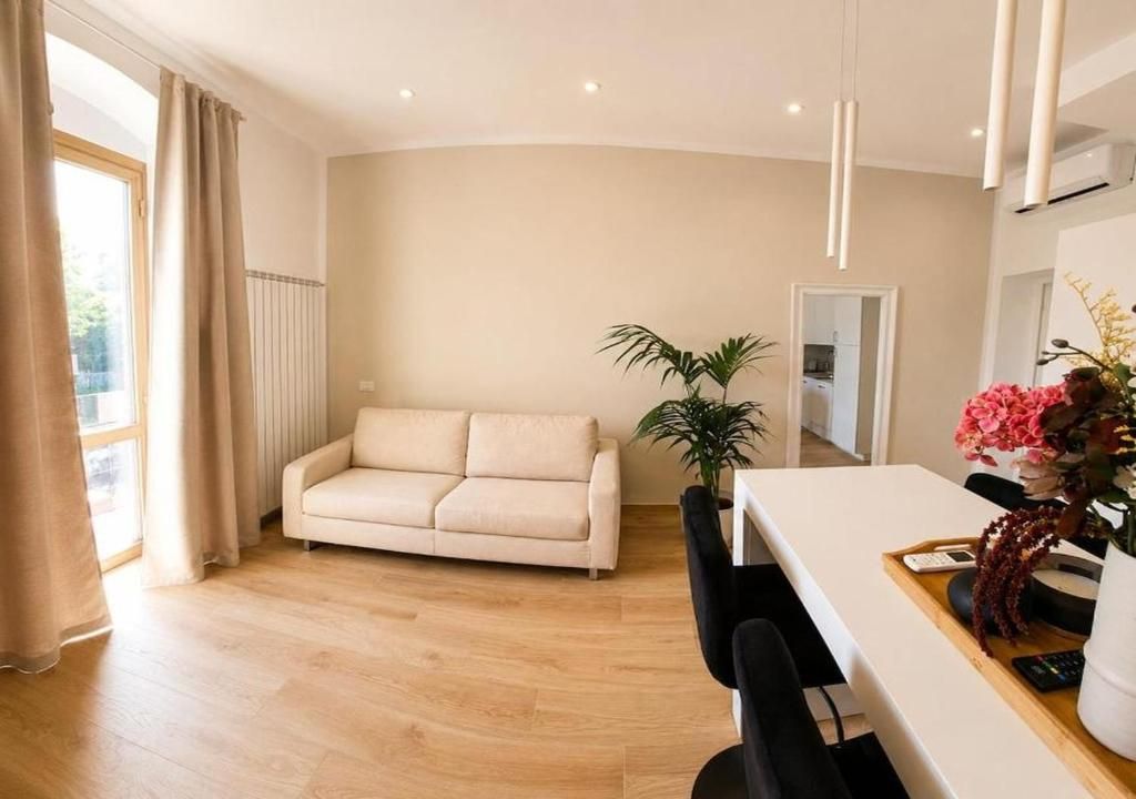 Un salon moderne avec un canapé beige, une table à manger avec des chaises, une plante en pot et un vase de fleurs.