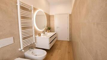 Un baño moderno con un lavamanos blanco, un espejo redondo, un perchero y un inodoro.